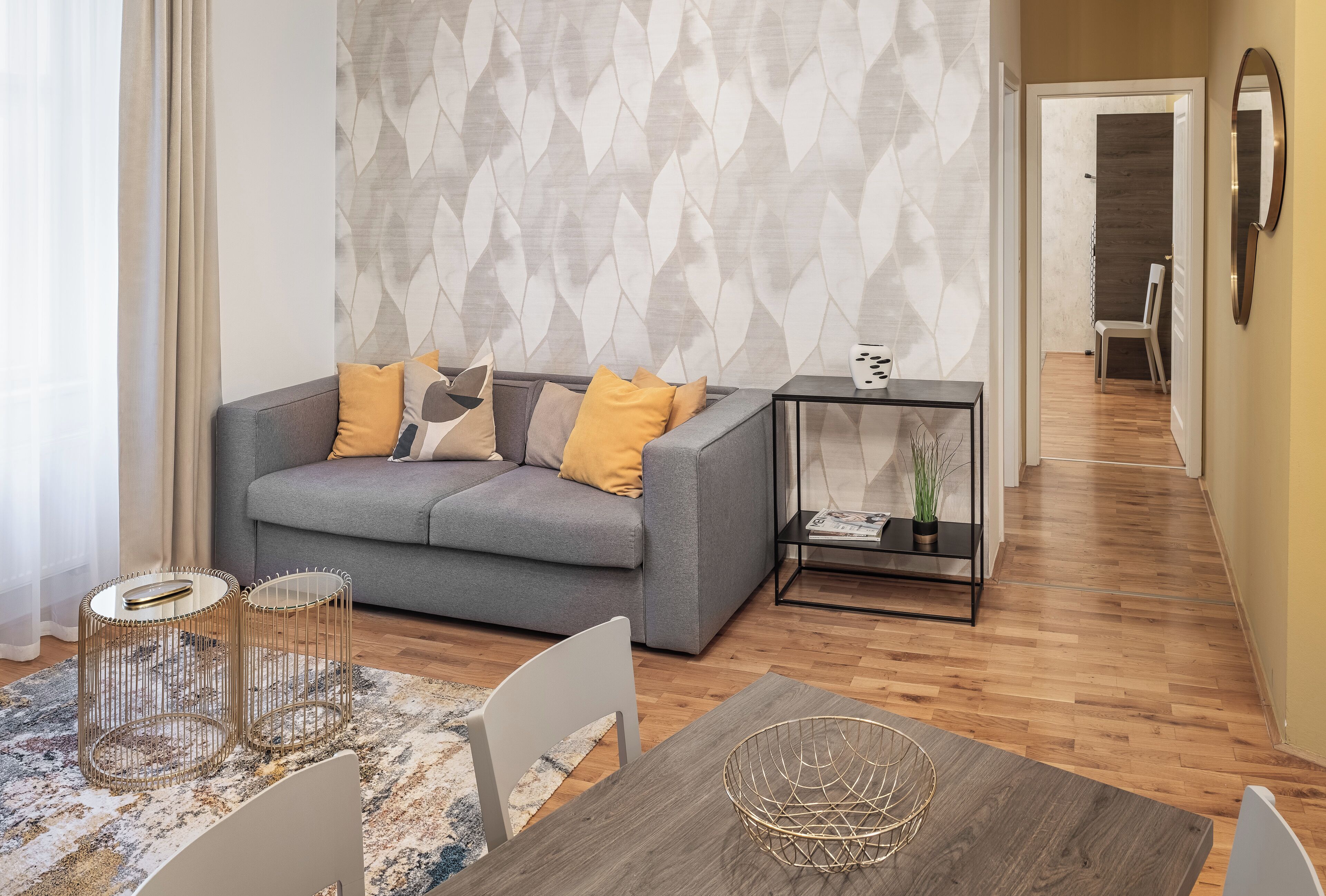 A modern living room with a grey sofa, yellow cushions, a wooden dining table, and a patterned rug.