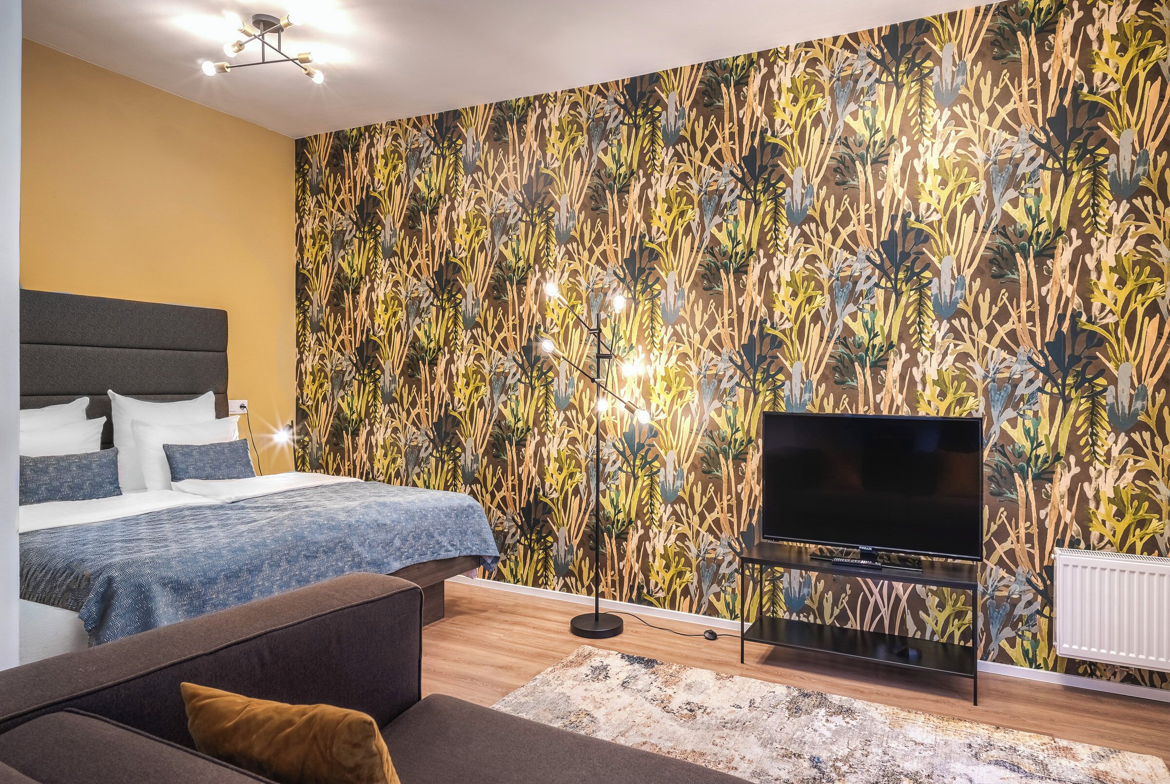 A modern bedroom with a large bed, a flat-screen TV, and a patterned wall.