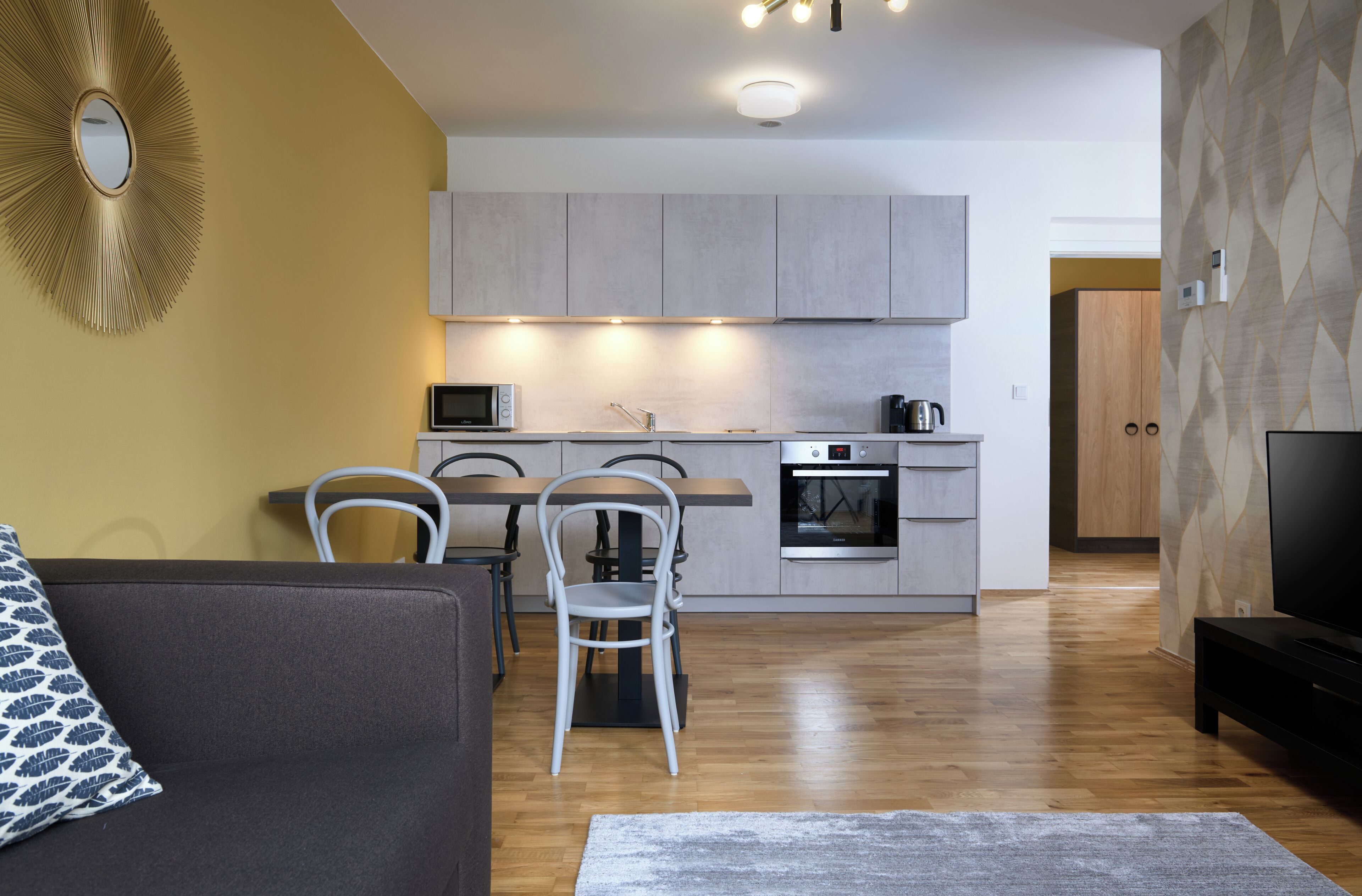 Una sala moderna con un sofá y sillas, una cocina con armarios y electrodomésticos, y un televisor en una esquina.