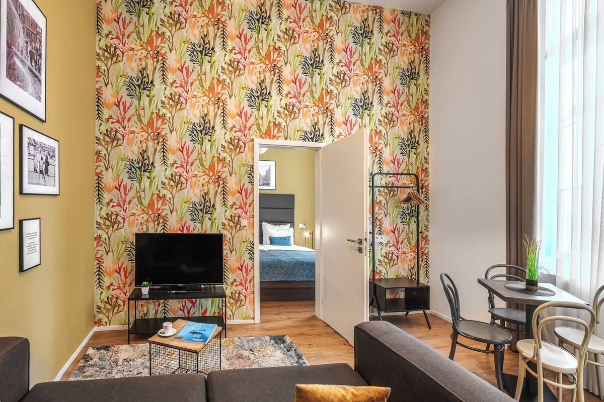 Uma sala de estar moderna com uma grande TV de tela plana, um sofá, uma mesa de centro e uma área de jantar com cadeiras.