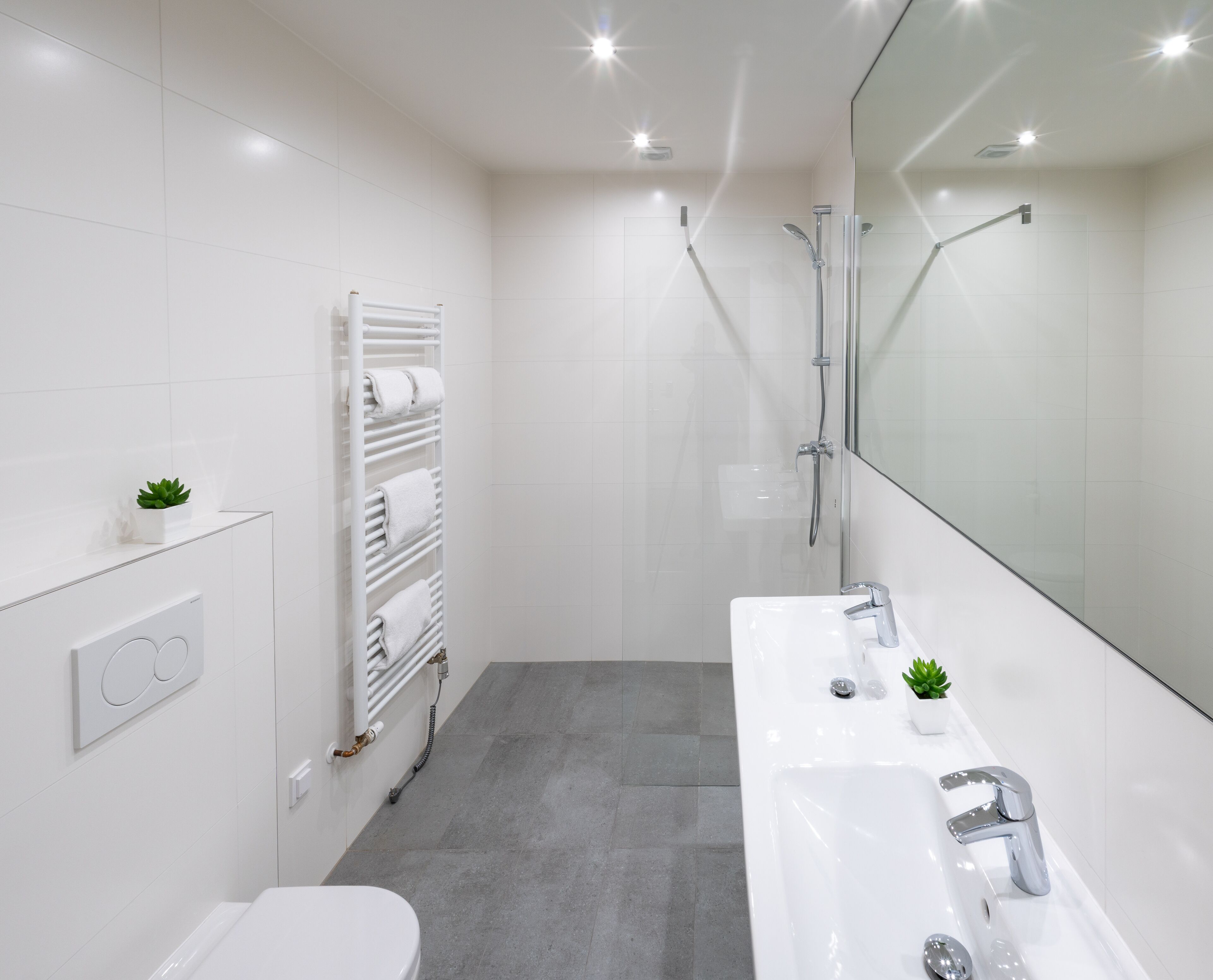 A modern bathroom with a white sink, a toilet, a glass shower enclosure, and a towel rack.