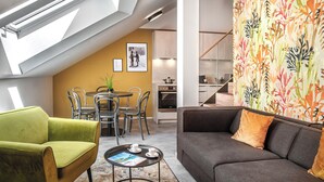 A modern living room with a green armchair, a gray sofa, and a coffee table. There is a dining area with a table and chairs, and a kitchen in the background. - VN48 Suites by Adrez Living (Prague)