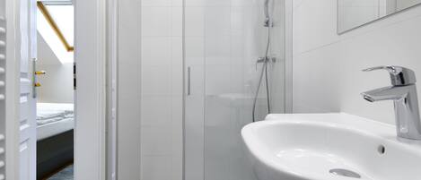 Ein modernes Badezimmer mit einer begehbaren Glasdusche, einem weißen Waschbecken und einem sichtbaren Bett im angrenzenden Raum.