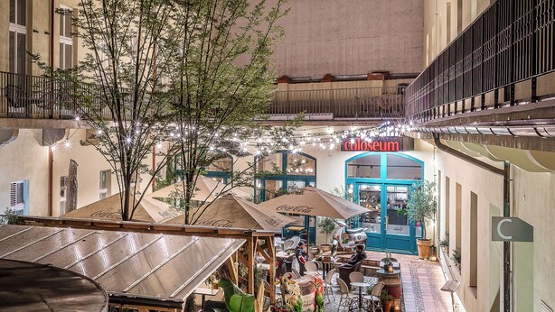 An outdoor café area with tables and chairs, surrounded by buildings and a blue door labeled "Coloseum". - VN48 Suites by Adrez Living (Prague)