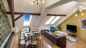 A dining area with a wooden table and chairs, a sofa, and a television. - VN48 Suites by Adrez Living (Prague)