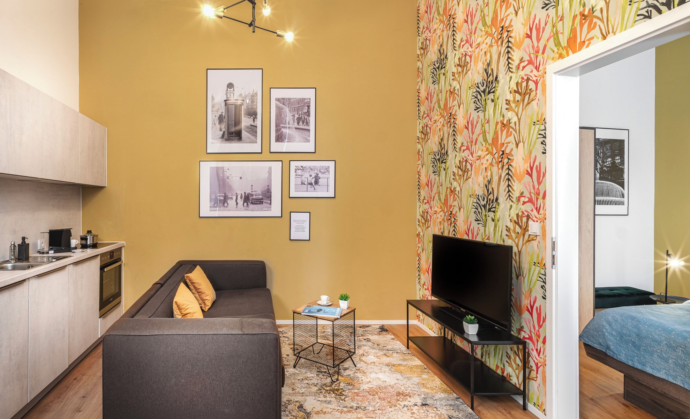Un espacio habitable compacto con kitchenette, un sofá, una mesa de centro, un televisor y un papel tapiz estampado.