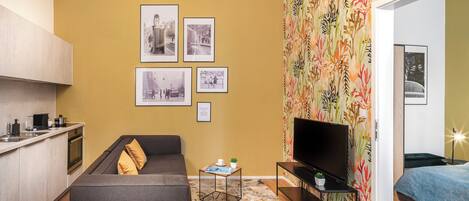 Un espacio habitable compacto con kitchenette, un sofá, una mesa de centro, un televisor y un papel tapiz estampado.