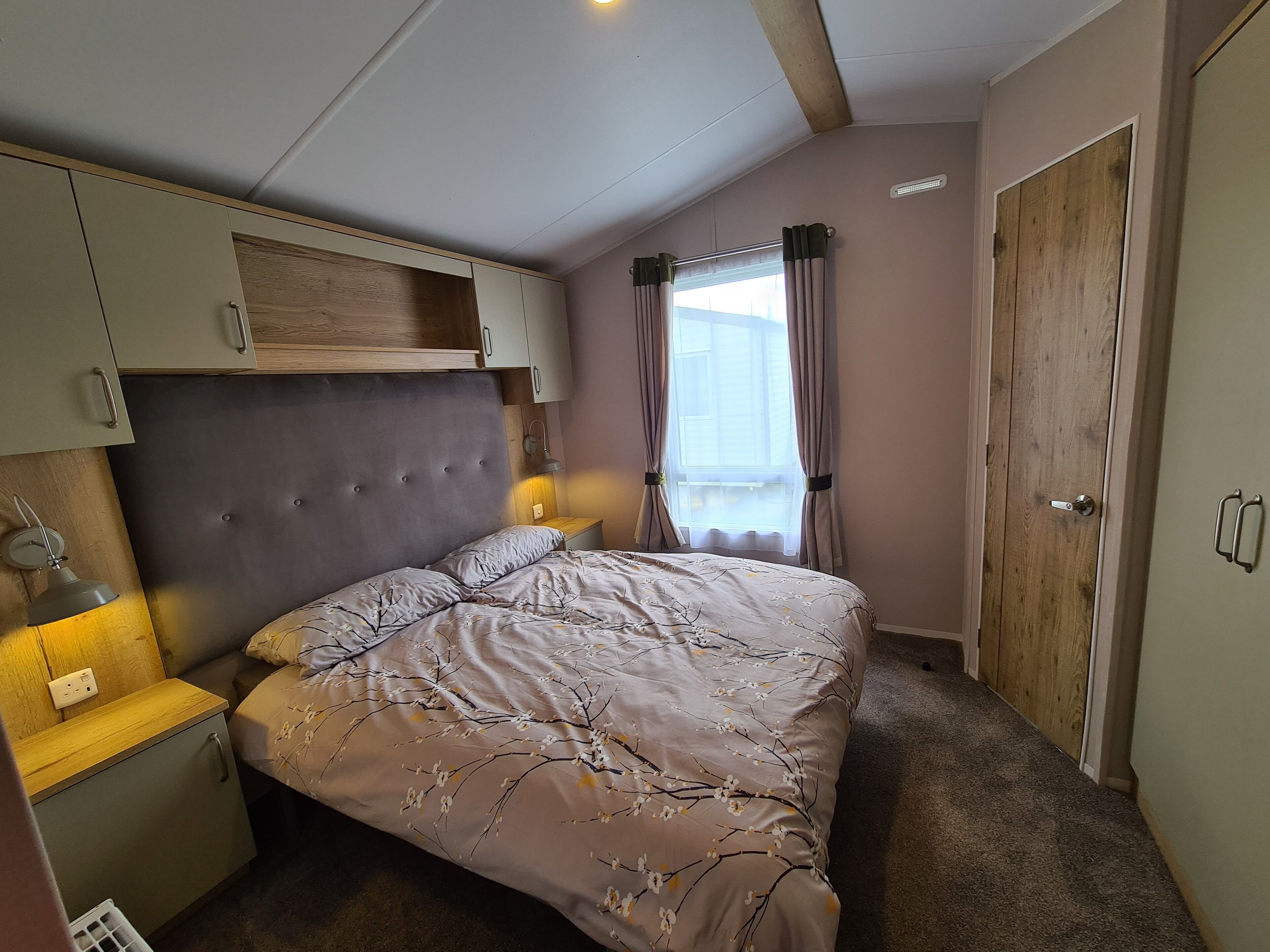 A bedroom with a bed, a nightstand, a wardrobe, and a window with curtains.