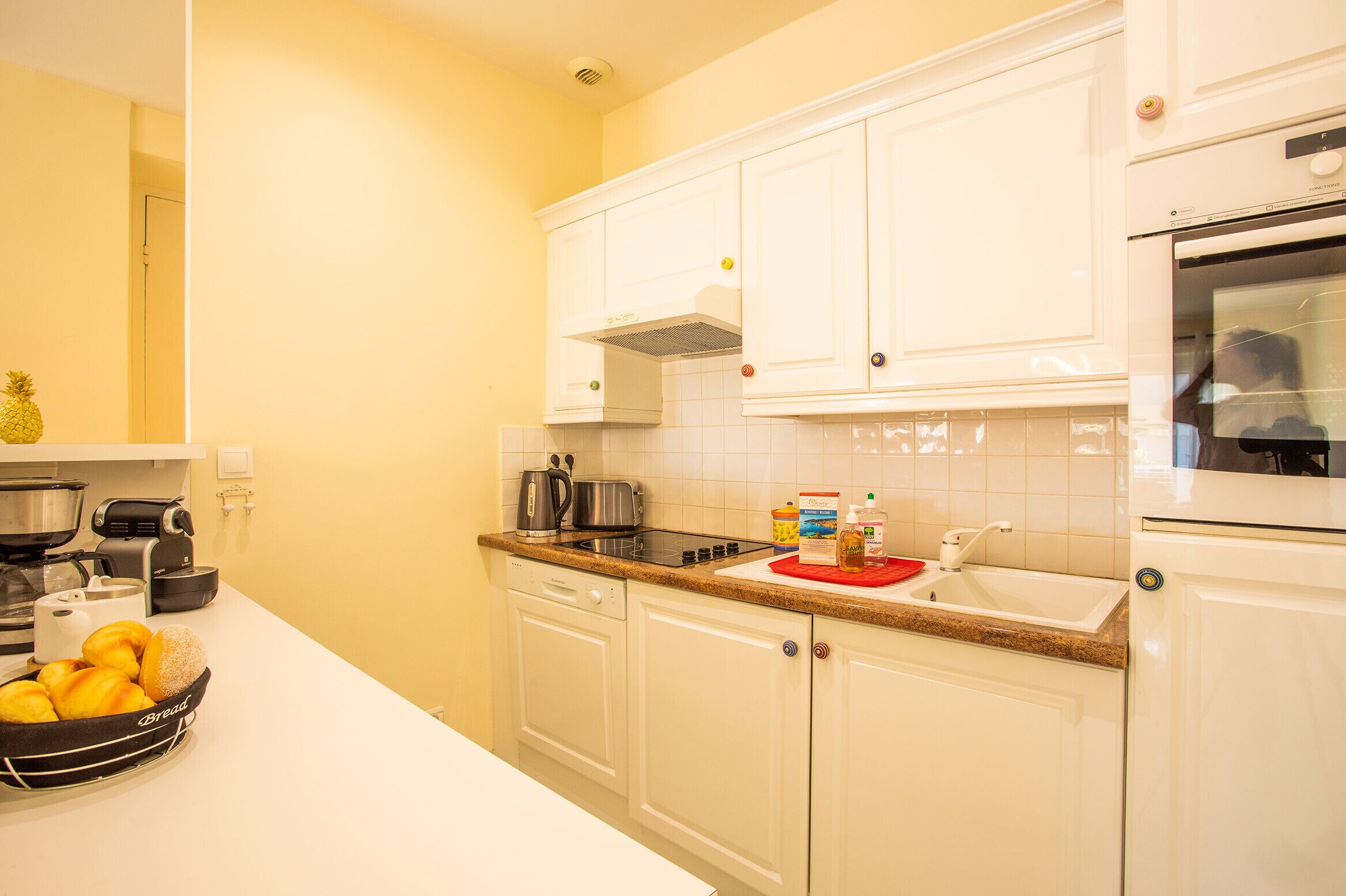 A kitchen with white cabinets, a countertop, a toaster, a kettle, and a bowl of bread.