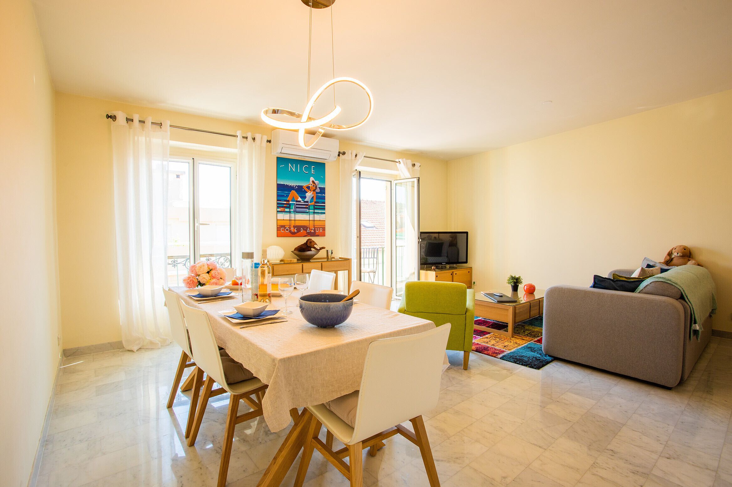 A modern living room with a sofa, a dining area with a table and chairs, a television, and a painting on the wall.