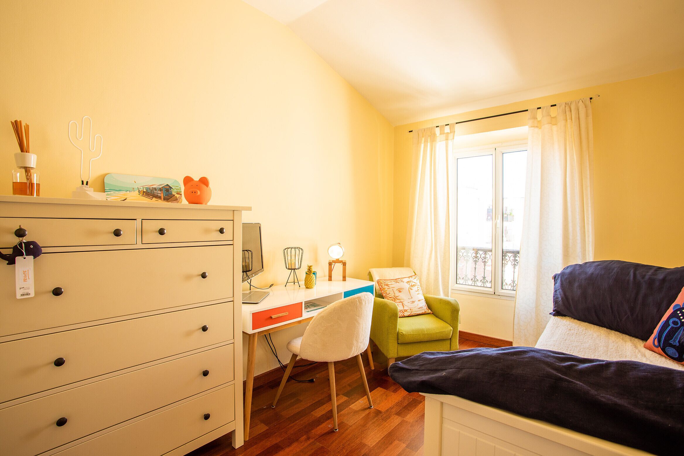 A room with a desk, chair, bed, and a window with curtains.