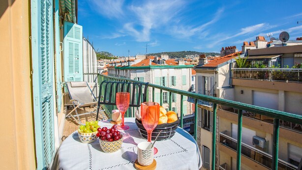 A balcony with a table set for two, featuring a bowl of grapes, a glass of red wine, and a basket of oranges. - LE FOCH AP4244 By Riviera Holiday Homes (Niza)