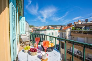 A balcony with a table set for two, featuring a bowl of grapes, a glass of red wine, and a basket of oranges. - LE FOCH AP4244 By Riviera Holiday Homes (Niza)