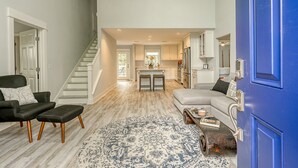 Tilava olohuone, jossa on portaikko, keittiö ja sininen ovi.