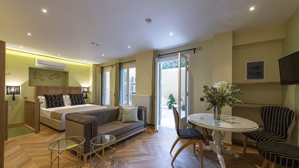 A modern hotel room with a bed, sofa, dining table, and chairs. - Ipelhome Plaka Boutique Apartments (Athens)