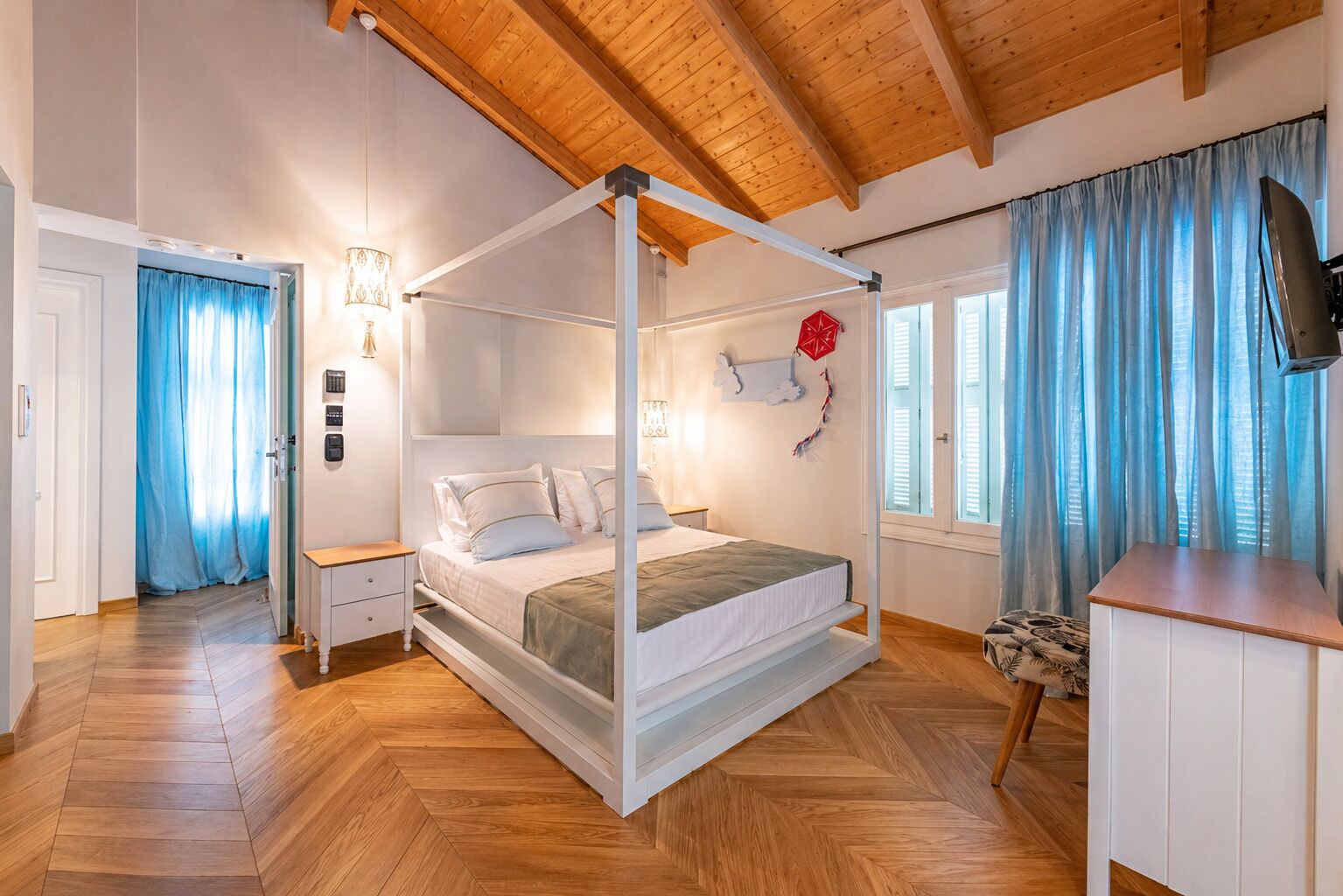 Un lit à baldaquin avec une literie blanche, un plafond en bois et un téléviseur sur le mur de droite.