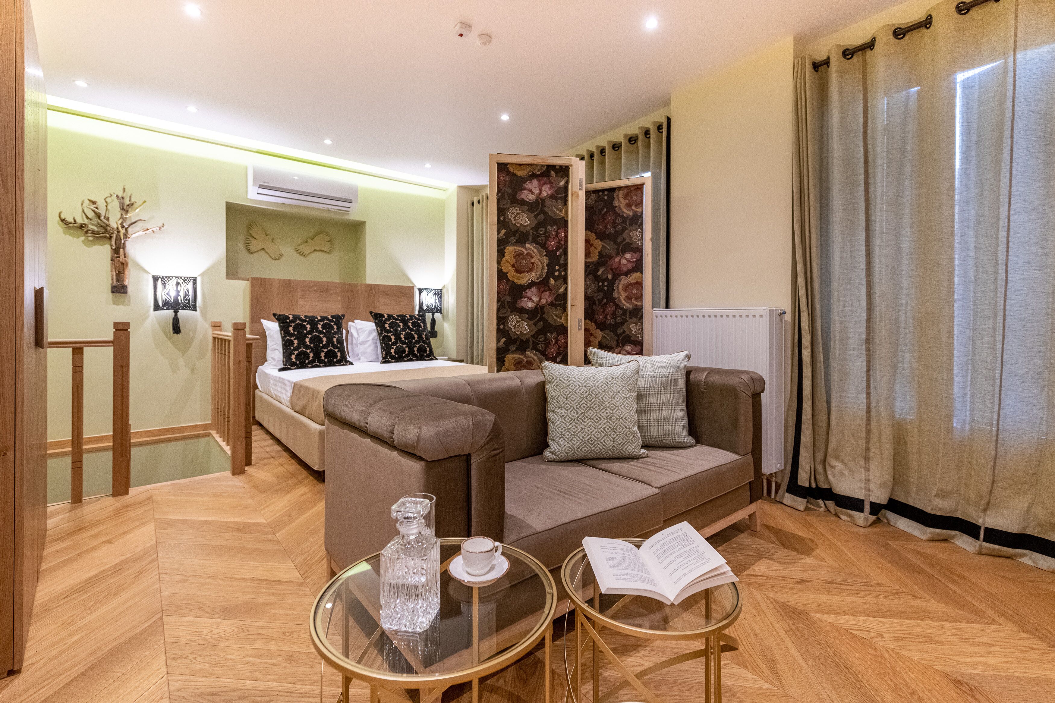 A modern hotel room with a bed, a sofa, a glass coffee table, and a reading area.