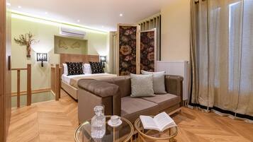 A modern hotel room with a bed, a sofa, a glass coffee table, and a reading area.