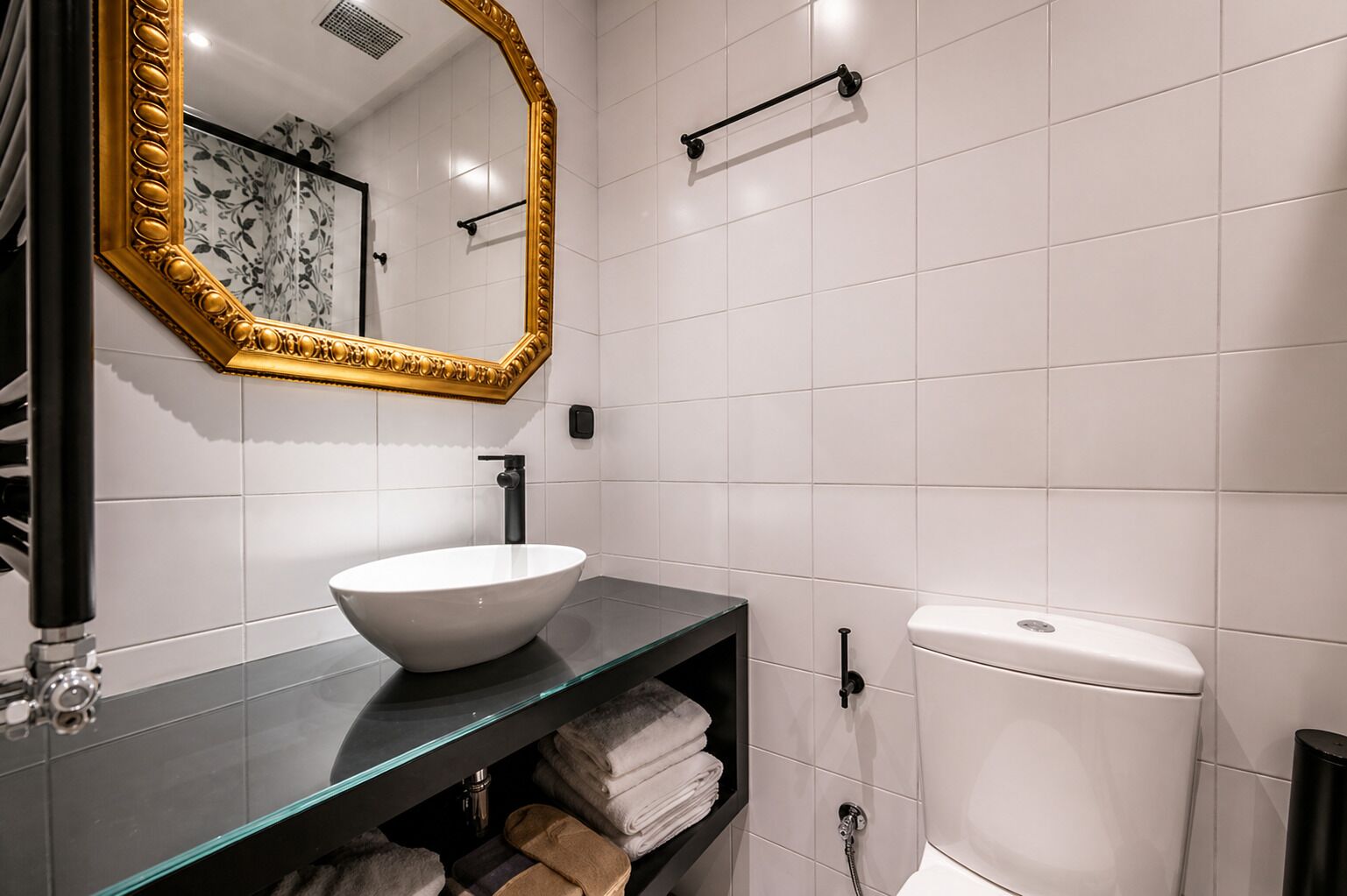 A bathroom with a white toilet, a glass sink, a gold-framed mirror, and a towel rack.