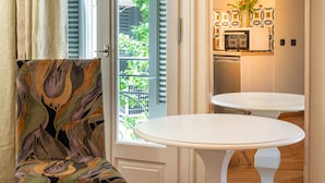 A room with a patterned armchair, a white table, and a view of greenery outside. - Ipelhome Plaka Boutique Apartments (Athens)