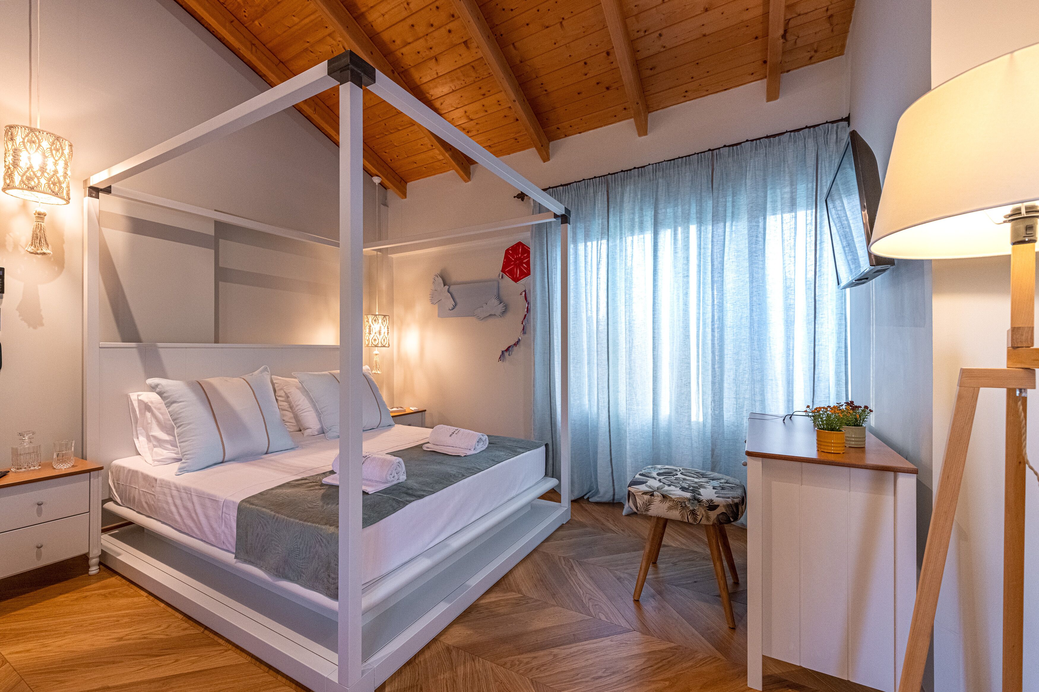 A bedroom with a four-poster bed, a nightstand, a bedside table, a chair, and a desk with a lamp.