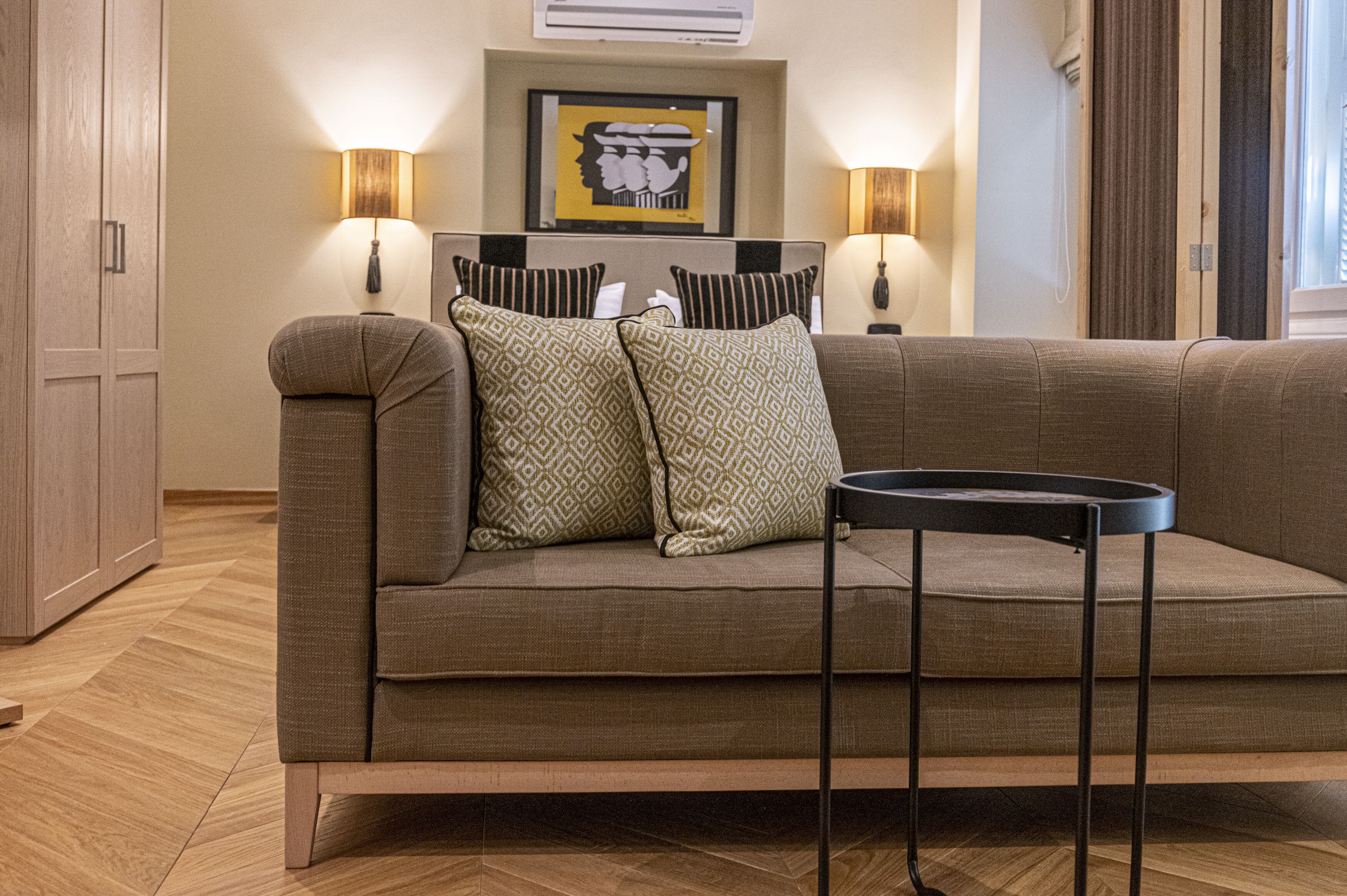 A modern living room with a sofa, two patterned pillows, a side table, and two wall-mounted lamps.