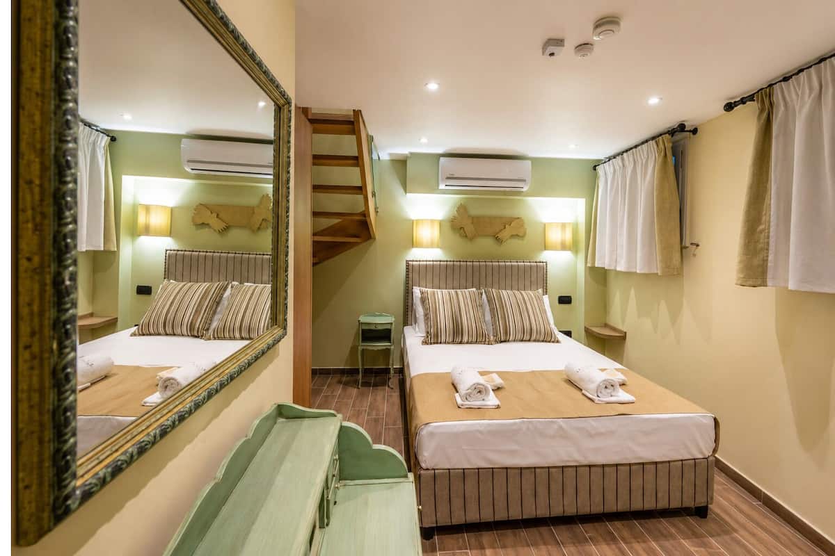 A hotel room with two beds, a mirror, a staircase, and an air conditioning unit.