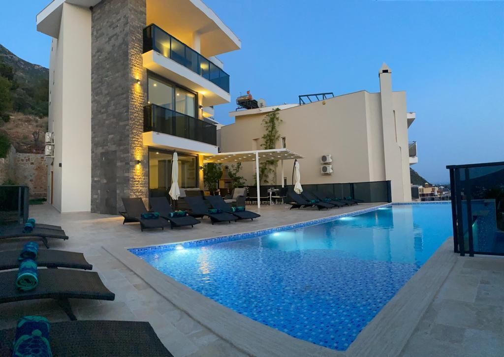 A modern building with a swimming pool, lounge chairs, and a covered seating area.