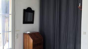 A room with a wooden dresser, a dark curtain, a hanging light fixture, and a window with sheer curtains.