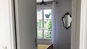 Une chambre à coucher avec un lit, une fenêtre, un miroir et une porte donnant sur une autre pièce.