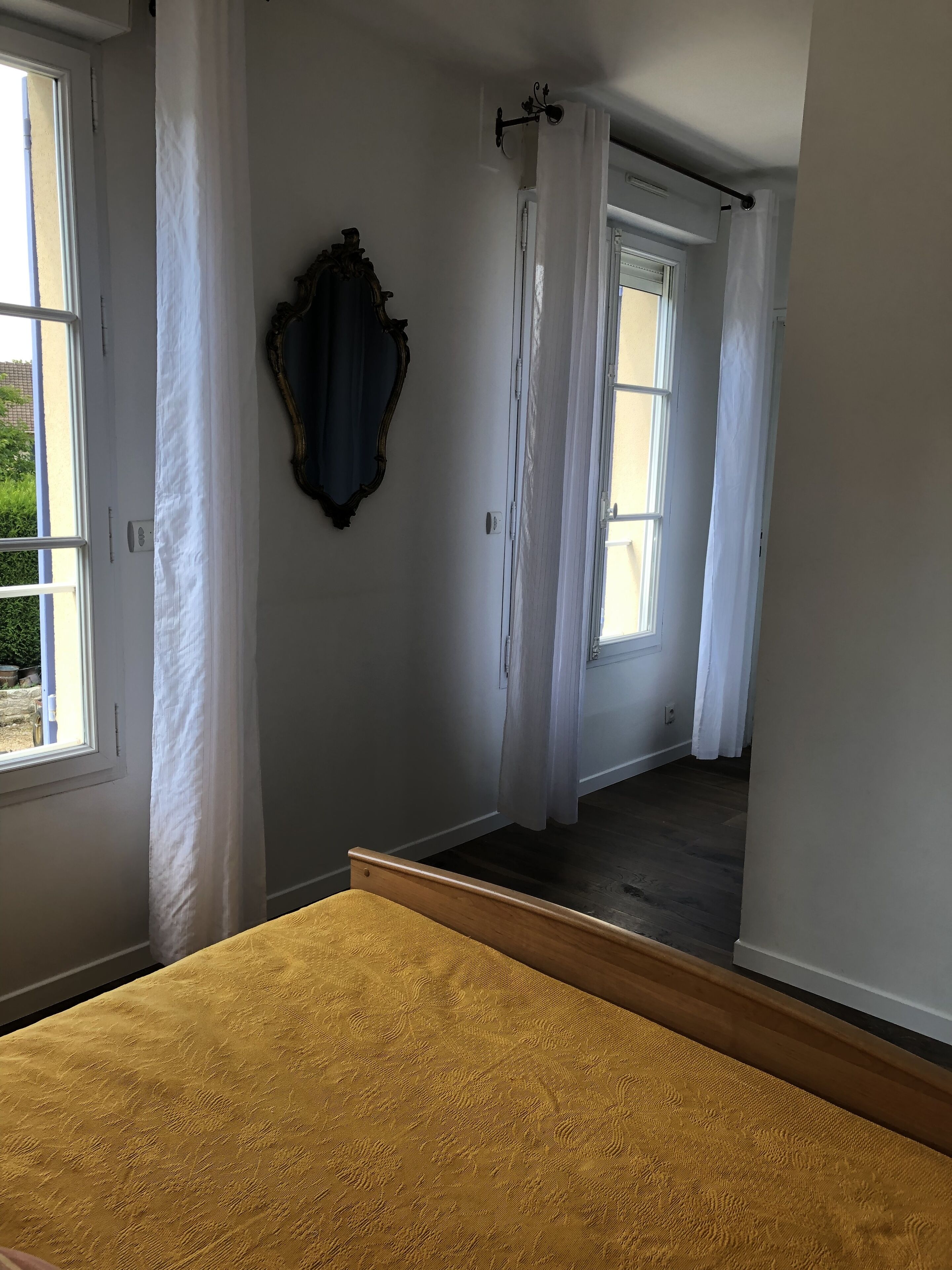 Una habitación con una cama, un espejo y dos ventanas con cortinas.