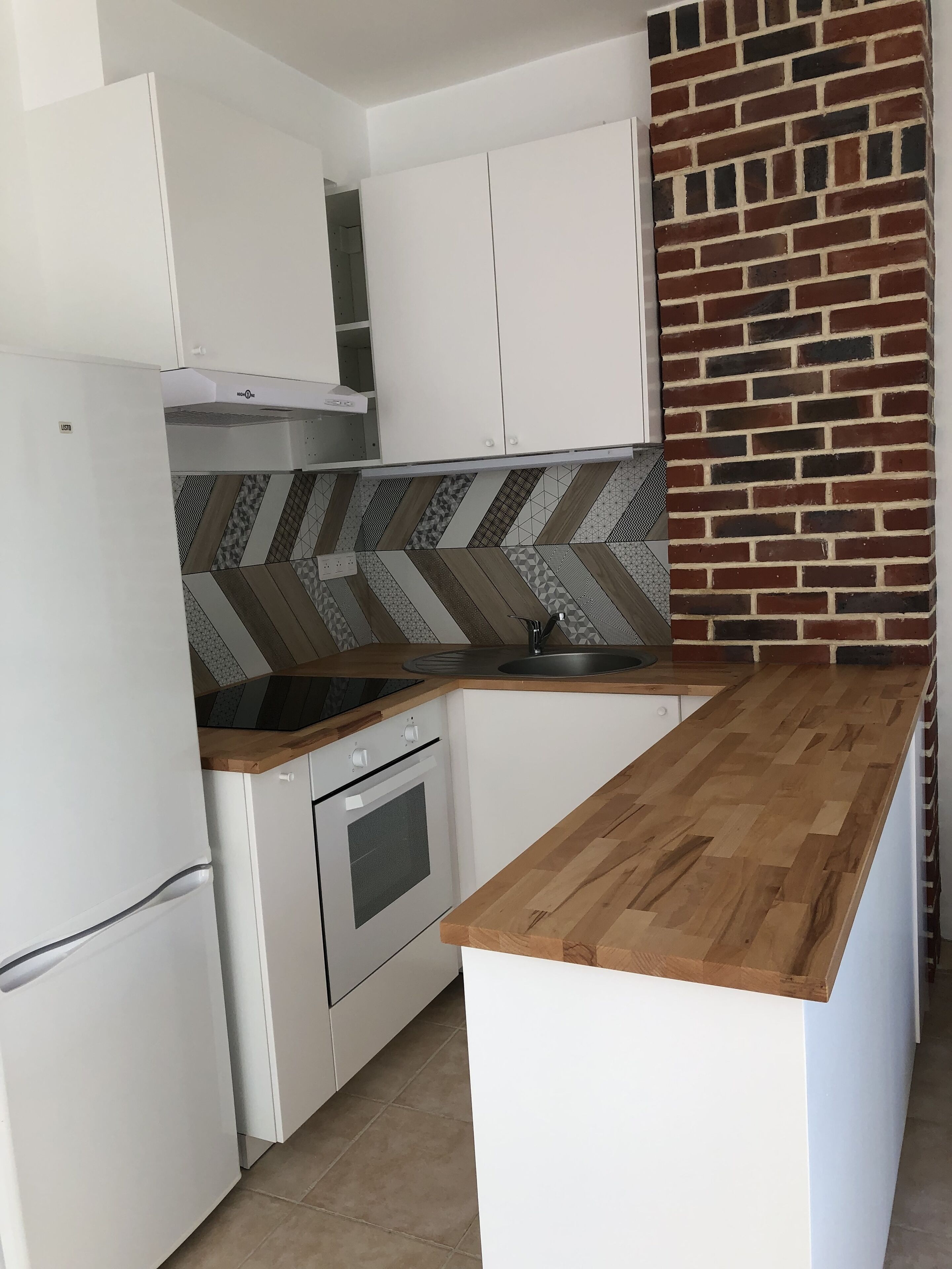 A modern kitchen with white cabinetry, a wooden countertop, a built-in oven, and a patterned backsplash.