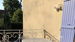 Une terrasse avec une table et des chaises en métal, un portail bleu et un mur muni d’un luminaire.