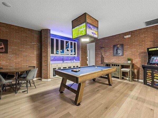 Una mesa de billar en una habitación con paredes de ladrillo, una zona de bar y una máquina de juegos.