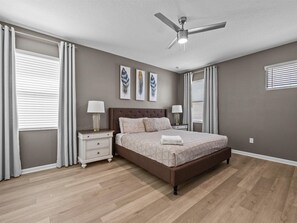 Un dormitorio con una cama, dos mesitas de noche, un ventilador de techo y cuadros en la pared.