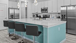 Une cuisine moderne avec des meubles blancs, des appareils en acier inoxydable et un îlot central doté de tabourets de bar.