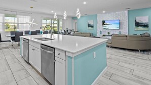 Une cuisine moderne avec un îlot central, un coin repas avec des chaises, un canapé et un mur dédié à la télévision.