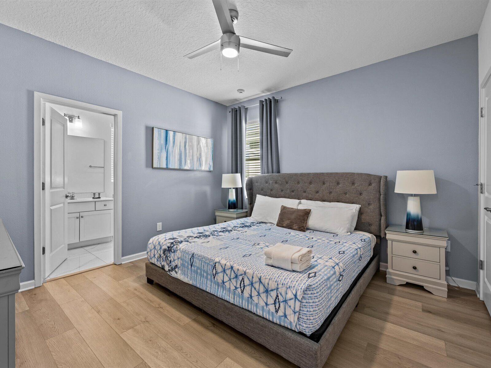 A bedroom with a bed, two bedside tables, a ceiling fan, and a door.