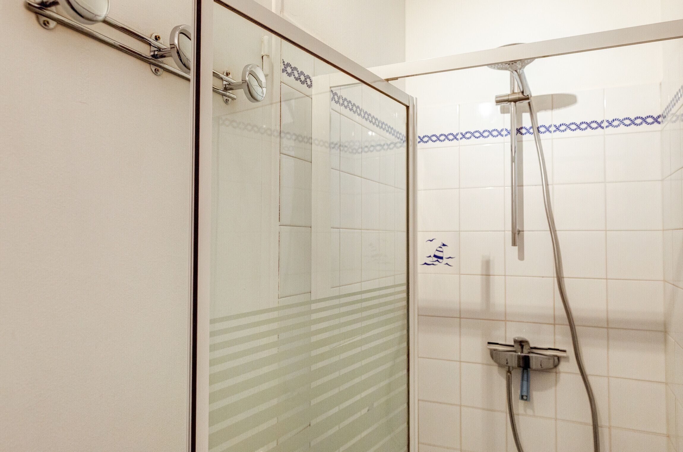 A glass-enclosed shower with a handheld showerhead and a wall-mounted faucet.