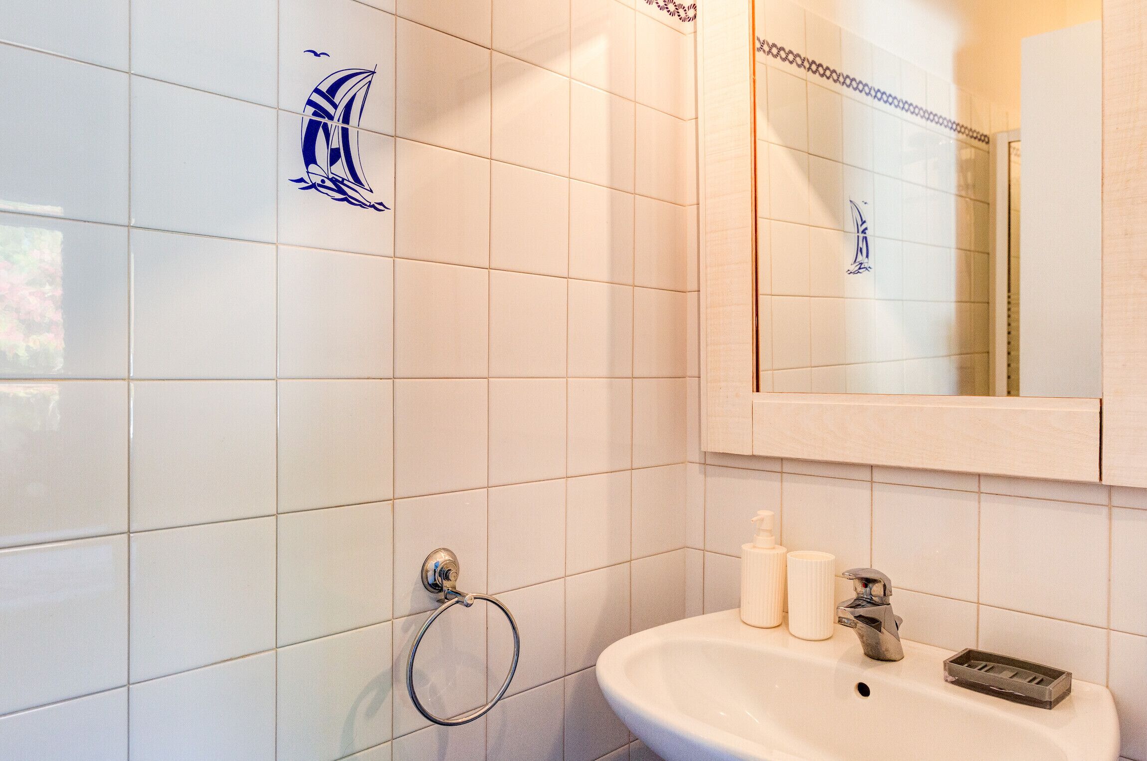 A bathroom with white tiles, a sink, a mirror, and a towel rack.