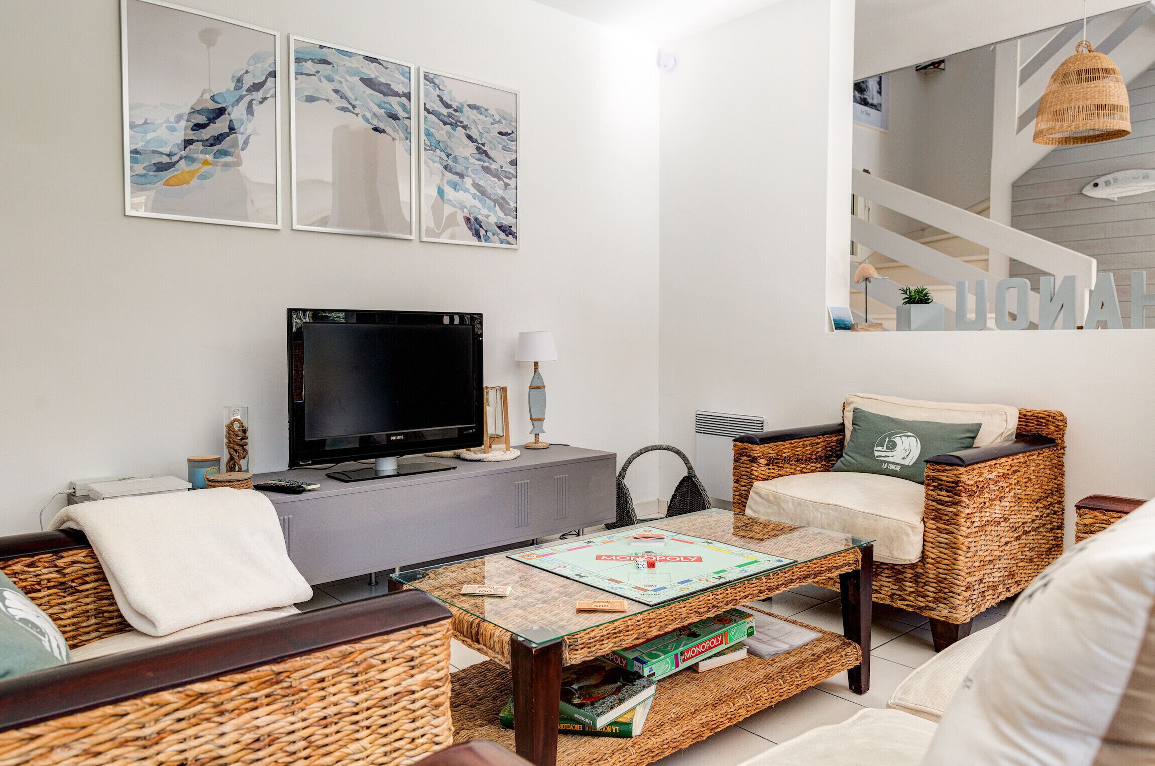 Un salón moderno con televisor de pantalla plana, mobiliario de mimbre y arte abstracto en la pared.