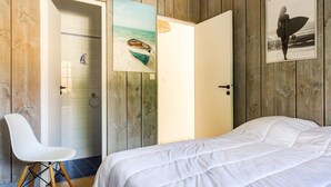 Una camera da letto con un letto, una sedia bianca, pareti in legno e una porta decorata con un'immagine a tema spiaggia.