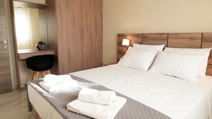 A neatly made bed with white linens and a quilted blanket, a wooden wardrobe, a small desk with a chair, and a bedside lamp. - Orea Homes (Parga)
