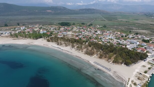 An aerial view of a coastal town with a beach, residential buildings, and a clear view of the surrounding landscape. - Orea Homes (Parga)