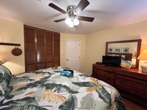 A bedroom with a bed, a ceiling fan, a dresser, a television, and a door. - Kamaole Beach Royale #304, Panoramic Ocean View of Kam Beach #1, Full Kitchen (Kihei)