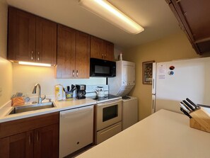 A compact kitchen with wooden cabinets, a dishwasher, a microwave, a stove, and a refrigerator. - Kamaole Beach Royale #304, Panoramic Ocean View of Kam Beach #1, Full Kitchen (Kihei)