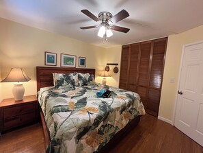 A bedroom with a bed, nightstand, lamp, ceiling fan, and a door. - Kamaole Beach Royale #304, Panoramic Ocean View of Kam Beach #1, Full Kitchen (Kihei)