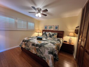 A bedroom with a bed, a ceiling fan, a nightstand, a lamp, and a window with blinds. - Kamaole Beach Royale #304, Panoramic Ocean View of Kam Beach #1, Full Kitchen (Kihei)