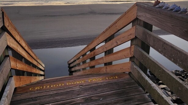 Una passerella di legno che conduce a una spiaggia, con un mare calmo e un tramonto sullo sfondo.
