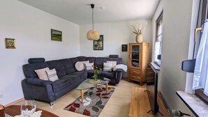 A modern living room with a dark grey sectional sofa, a glass coffee table, and a wooden cabinet.